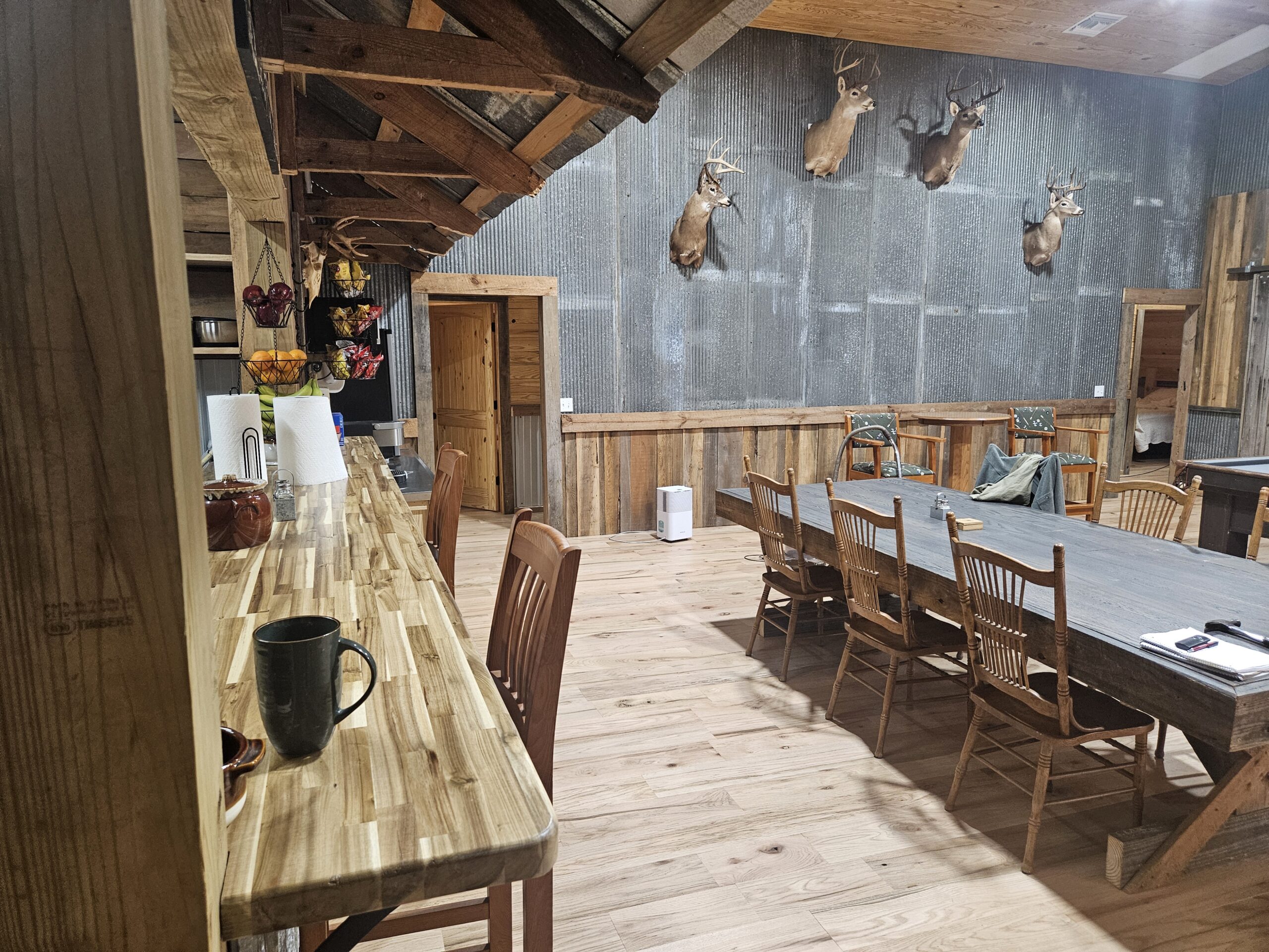Rustic Lodge Dining Area Featuring a Long Wooden Table, Bar Counter, and Mounted Deer Heads on the Wall