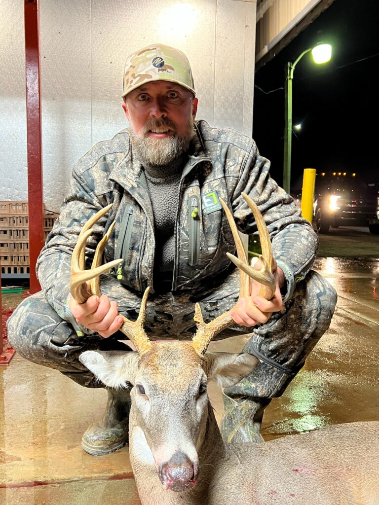 Hunter in Camouflage Clothing Kneeling Beside a Harvested White-Tailed Deer at Night