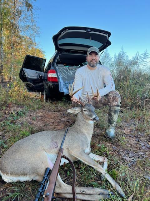 A Hunter Kneeling Beside a Harvested Deer with a Rifle Resting Nearby